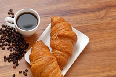 Masanın üzerinde bir fincan espresso ve çıtır çıtır iki kruvasan var..