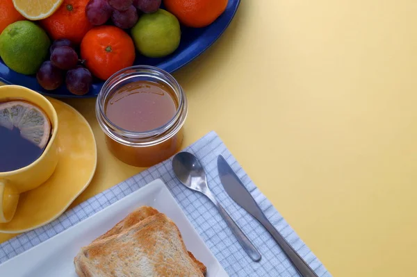 黄色阳光充足的背景会增加食欲 早餐吃吐司加果酱或蜂蜜 再加上茶和水果 是一天中最好的开始 — 图库照片