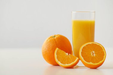 Yatay bir fotoğraf taze sıkılmış bir bardak portakal suyu ve taze ve sulu portakalların tamamını gösteriyor. Enerji dolu, C vitamini ile zenginleştirilmiş güne mükemmel bir başlangıç ve iyi bir kahvaltı.