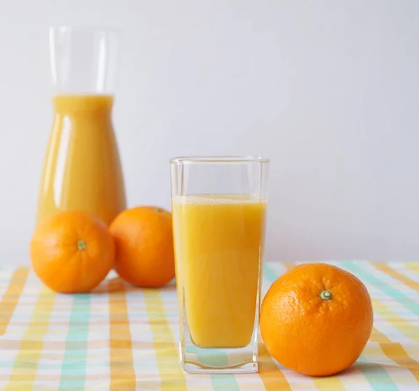 美しいテーブルクロスとテーブルの上にはガラスと新鮮な絞りオレンジジュースのジャグが立っており 新鮮なオレンジが近くにあります 一日中エネルギーとビタミンの充電 — ストック写真