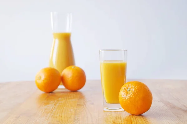 木製のテーブルの上に新鮮なオレンジジュースを用意したガラスがあり ジュースの瓶が隣に立っています オレンジもテーブルにあります ビタミンCの充電と一日の陽気さ — ストック写真