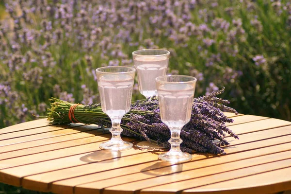 Three glasses of lavender cocktail are on the table, next to it lies a bouquet of lavender flowers. The table stands in a lavender field. Excellent atmosphere for relaxation, self-knowledge, rest, recovery of health - lavender aromatherapy