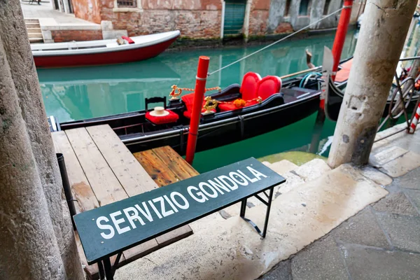 運河で観光客を待っているイタリアのヴェネツィアのゴンドラ 手前にはゴンドラの運行案内が書かれている ヴェネツィアの古代ポルティコの隣にゴンドラの着陸場所 — ストック写真