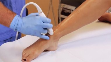 Kadın bir hastaya ayak bileği ekleminde ultrason yapan bir doktor. Bir hekim tarafından ön bilek ultrasonu muayenesi. Tendonları ve bilek eklemini incelemek için bir doktor tarafından ayak ultrasonu muayenesi..