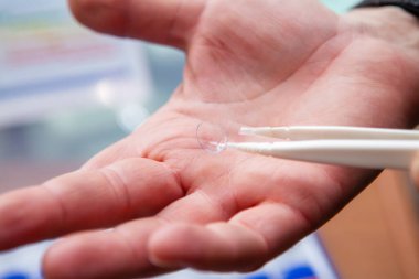 Erkek bir gözlükçü, cımbız kullanarak avucunun içinde duran temiz ve temiz bir lens gösterir.