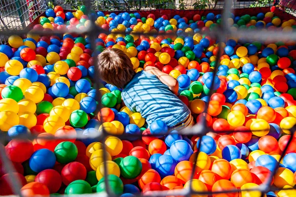 A child plays in a ball pool filled with colorful plastic balls on a playground