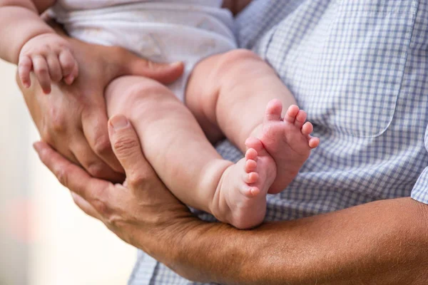 Bir baba yeni doğmuş bir bebeği kucağında tutuyor. Baba ve yeni doğan kız. Bir adamın elleri, bacakları ve yeni doğmuş bir bebeğin küçük ayakları..