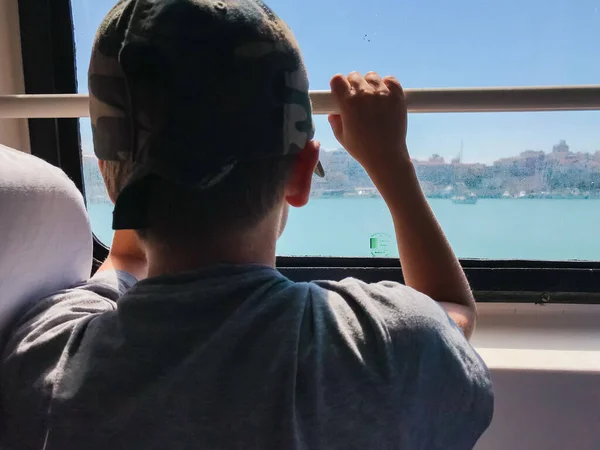 Feribotta yalnız bir çocuk pencereden mavi denize bakıyor.