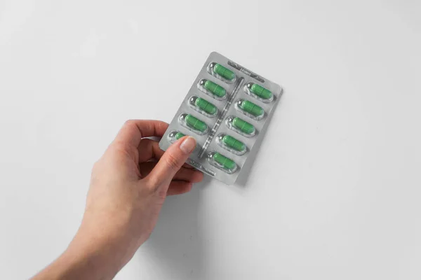 Womans hand holds silver blister with supplements in green capsules on white background. Sedative pills. — Stock Photo, Image