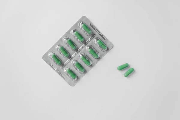 Blister in argento con integratori e vitamine in capsule verdi su sfondo bianco. Concetto sanitario. Vista dall'alto. — Foto Stock
