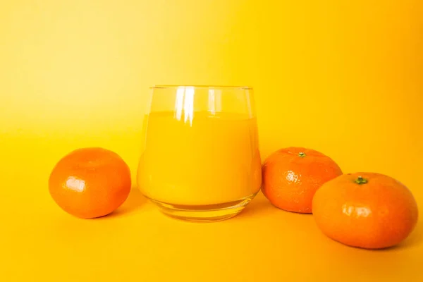 Стакан свежего апельсинового сока с тремя цитрусовыми фруктами мандарина рядом. Изолированный на желтом фоне. — стоковое фото