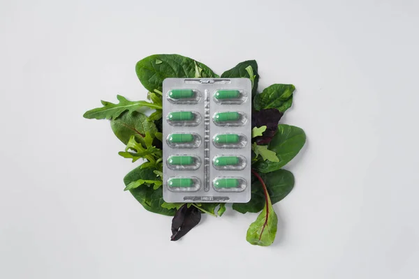 Blister de plata con suplementos dietéticos en cápsulas verdes en las hojas verdes de rúcula y lechuga. Concepto de salud. — Foto de Stock