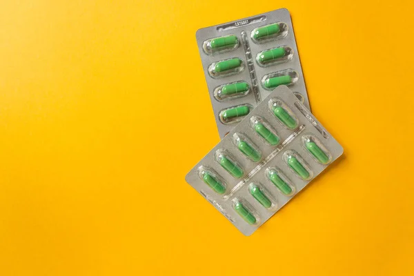 Two silver blisters with supplements and vitamins in green capsules on yellow background. Health care concept.