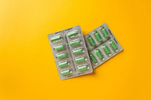 İki gümüş kabarcık, takviyeli ve yeşil kapsüllü vitaminler, sarı arka planda. Sağlık hizmeti kavramı. — Stok fotoğraf