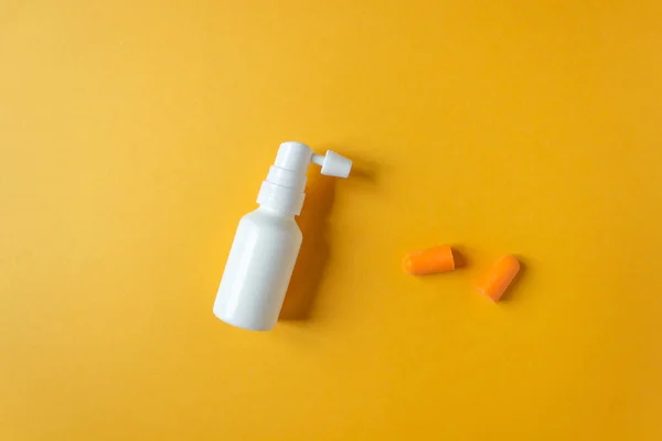 Vista superior de la botella pulverizadora de oreja blanca con boquilla y tapones anaranjados aislados sobre fondo amarillo. Cuidado diario de los oídos. — Foto de Stock