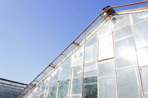 Antiga estufa destruída com vidros quebrados e moldura enferrujada. Geometria urbana arruinada. Céu azul. — Fotografia de Stock