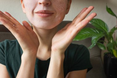 Yüzünün yarısı kilden bir kozmetik maske takıyor. Evde yüz maskesi takmak. Yüz bakımı konsepti.