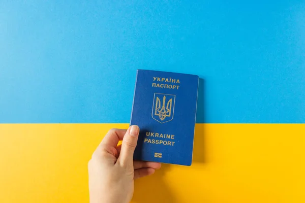 Mão das mulheres segurar Ucrânia passaporte biométrico na bandeira nacional da Ucrânia. Cores azul e amarelo. Imigração. — Fotografia de Stock