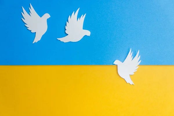 Three white paper dove birds as a symbol of peace on the background of the national flag of Ukraine. Peace to Ukraine. Stop war. Freedom, hope and International Day of Peace in september concept.