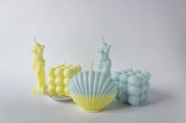 Baloncuk küpünde bir grup soya mumu, deniz kabuğu ve Venüs formu. Sarı ve mavi renklerde. Beyaz arkaplan.
