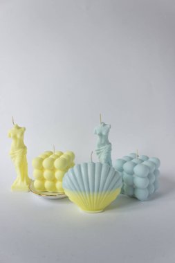 Baloncuk küpünde bir grup soya mumu, deniz kabuğu ve Venüs formu. Sarı ve mavi renklerde. Beyaz arkaplan.