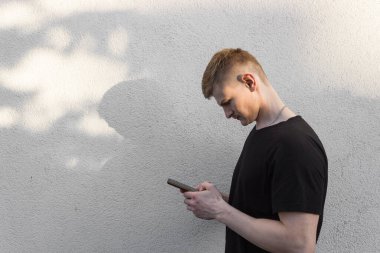 Siyah tişörtlü, akıllı telefon kullanan beyaz sarışının profili. Milenyum çocuğu sosyal medyada sohbet ediyor, mobil servisin tadını çıkarıyor. Beyaz arka planda izole edilmiş. İnsanlar ve aletler. 