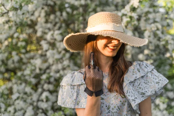 Brunette woman in straw hat showing middle finger in vintage black lace glove with luxury ring and smiles. Fuck off sign to seasonal allergy. Fuck off to my vacation in this year.