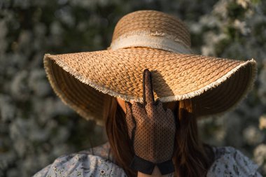 Young woman in straw hat showing middle finger in vintage black lace glove. Fuck off sign to seasonal allergy. Feminist gesture against war. Stop war in Ukraine.