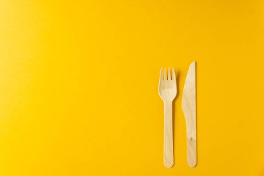 Doğal malzemelerden tek kullanımlık sofra takımı. Sarı arka planda bulunan ahşap çatal ve bıçak. Üst Manzara. Çevre dostu materyaller. Plastiksiz konsept.