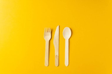 Doğal malzemelerden tek kullanımlık sofra takımı. Sarı arka planda bulunan bambu ahşap çatal, kaşık ve bıçak. Üst Manzara. Çevre dostu materyaller. Plastiksiz konsept.