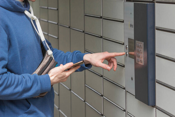 Pniewy, Poland - 22 May 2022. Man with smartphone entering code to open shopping locker in inPost delivery service. E-commerce shipping and delivery. People and gadgets concept.
