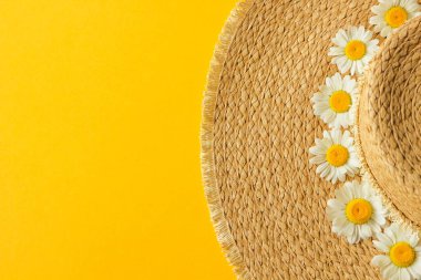 Sarı arka planda izole edilmiş papatya çiçekleri ile süslenmiş samandan yapılmış güneş şapkası. Yaz plajı tatili konsepti. Yaz satış konsepti.
