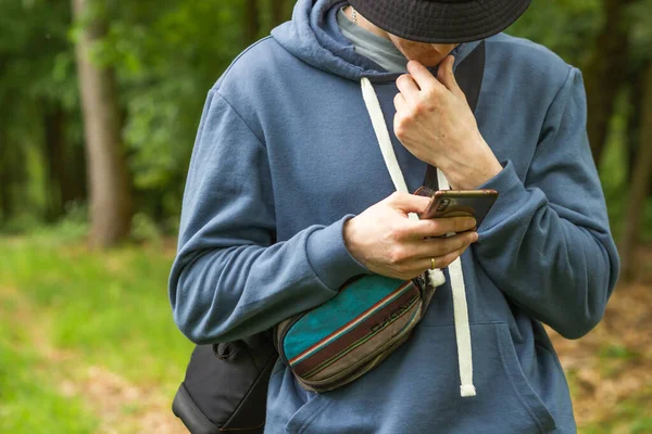 Turist akıllı telefon kullanarak mavi kapüşonlu sweatshirt giyer. Düşünceli bir adam çenesine elle dokunuyor, sosyal medyada sohbet ediyor, mobil servisin tadını çıkarıyor. Turist rotası çiziyor. İnsanlar ve aletler. 