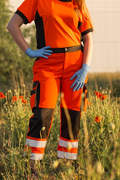 Polish ambulance worker standing in medical orange uniform with reflective elements and blue gloves on hands. Technician or doctor of Emergency medical Services in Poland.