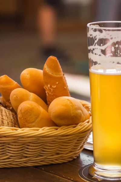 Glass of light beer and bread basket with different pastries on the wooden table at a craft czech brewery. Starter set to weekend meeting with friends. Alcoholic mans drink. Oktoberfest concept.