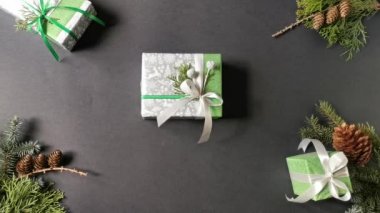 Gift-box wrapping in green and silver festive paper isolated on the black background with spruce cones, branch of spruce and gift-boxes. Preparing for Christmas holidays. DIY and handmade concept.