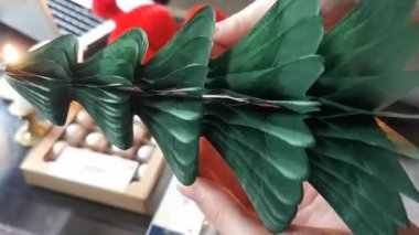 Womans hands unfold a paper Christmas tree. Handmade foldable plastic free decor. Concept of winter creativity and christmas crafts. Trendy eco Christmas trees. DIY concept.