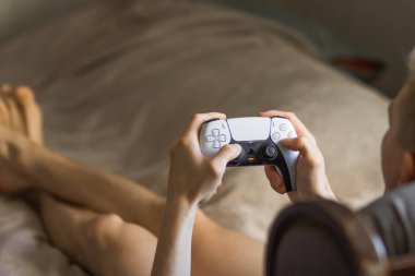 Poznan, Polonya - Ağustos 2022. Elinde Play Station 5 Dual Sense kumandası olan ve evdeki oyun konsolunda oyun oynayan genç bir adam. Hafta sonları boş zaman aktivitesi konsepti. Oyuncu yaşam tarzı.