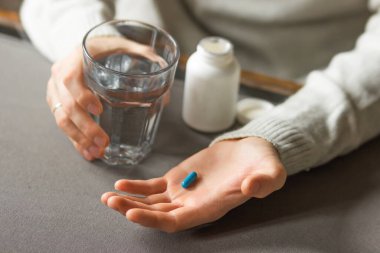 Mans hands holds a blue capsule and glass of water over the table, ready to take medicines. Sick man need medicine from headache and cold, painkiller, nutritional supplement. Health care concept. 