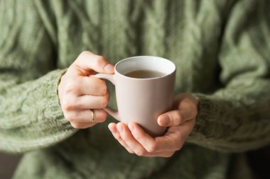 Married man wearing green knitted woolen sweater holding hot cup of tea in the cold autumn or winter morning. Mug for your design. Coffee or tea mug in male hands. Cozy at home. Heating season concept