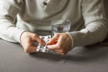 Mans hands holds and open silver blister with pills, and ready to take medicines with glass of water. Sick man need medicine from headache and cold, painkiller at home. Health care concept.
