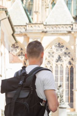Prag 'ın eski kenti Çek Cumhuriyeti' nin sokaklarını gezen beyaz tişörtlü, büyük siyah sırt çantalı genç adam. Gotik tarzda eski binaya bakıyorduk. Turizm ve seyahat kavramı. 