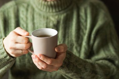 Married man wearing green knitted woolen sweater holding hot cup of tea in the cold autumn or winter morning. Mug for your design. Coffee or tea mug in male hands. Cozy at home. Heating season concept