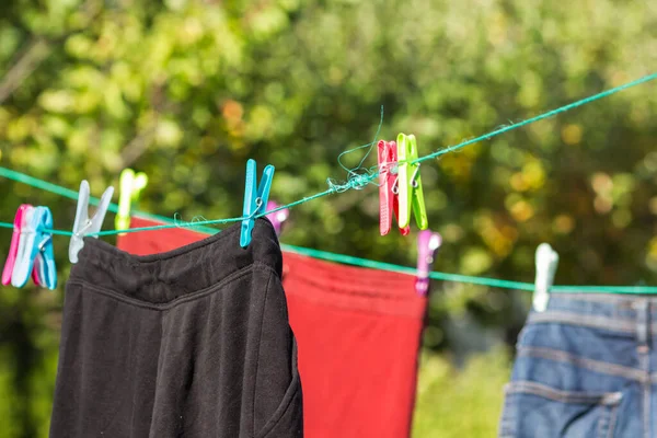 Clean laundry hangs and dries on a rope outside with plastic colorful clothespins. Organic drying clothes and jeans in a sunny autumn day. Home routine and cottagecore concept. Energy crisis concept.