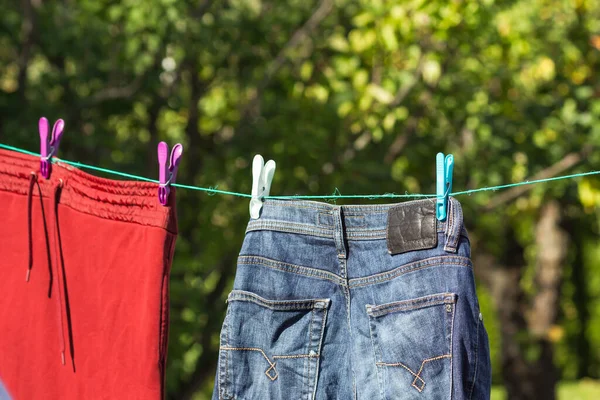 Clean laundry hangs and dries on a rope outside with plastic colorful clothespins. Organic drying clothes and jeans in a sunny autumn day. Home routine and cottagecore concept. Energy crisis concept.