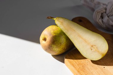 Olgun Konferans armutlarıyla dolu natürmort, tahta kesme tahtasıyla ikiye bölünmüş. Modaya uygun kontrastlı ışık, beyaz arka plan. Sonbahar tarifleri için. Sağlıklı beslenme ve vejetaryen konsepti.