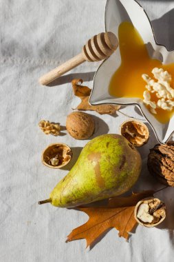 Kelebek şeklinde ballı ve kabuklu cevizlerle dolu sonbahar kompozisyonu beyaz kumaş zemin üzerinde olgun yeşil armut, ahşap bal kaplaması ve kuru meşe yaprakları. Konforlu ev konsepti. Üst görünüm.