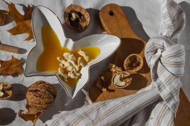 Kelebek şeklinde bal ve kabuklu ceviz içeren sonbahar kompozisyonu beyaz kumaş zemin üzerinde ahşap kesim tahtası, ceviz ve kuru meşe yaprakları. Konforlu ev konsepti. Üst görünüm.