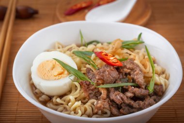 Tavuk, şehriye, yumurta, acı biber ve fasulye karışımı beyaz bir tabakta kaşık ve yemek çubuğu olan bir hasırla erişte çorbası. Asya sokak yemekleri.