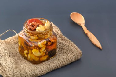 Ceviz, kaju, kuru üzüm, kurumuş kayısı ve kuru erik karışımı. Cam bir kavanozda bal ve gri bir masada kaşık.